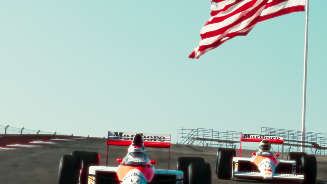 Two McLaren Formula 1 cars crest a hill beneath an American flag at Circuit of the Americas